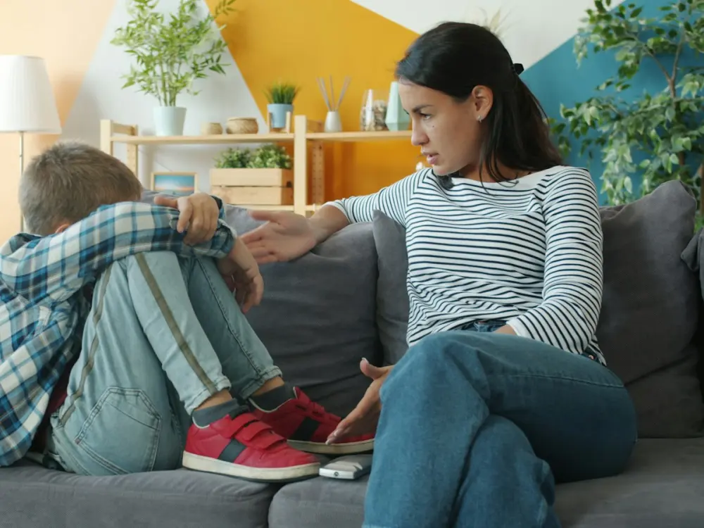 A boy curled up on the sofa after an argument, his mother beside him
